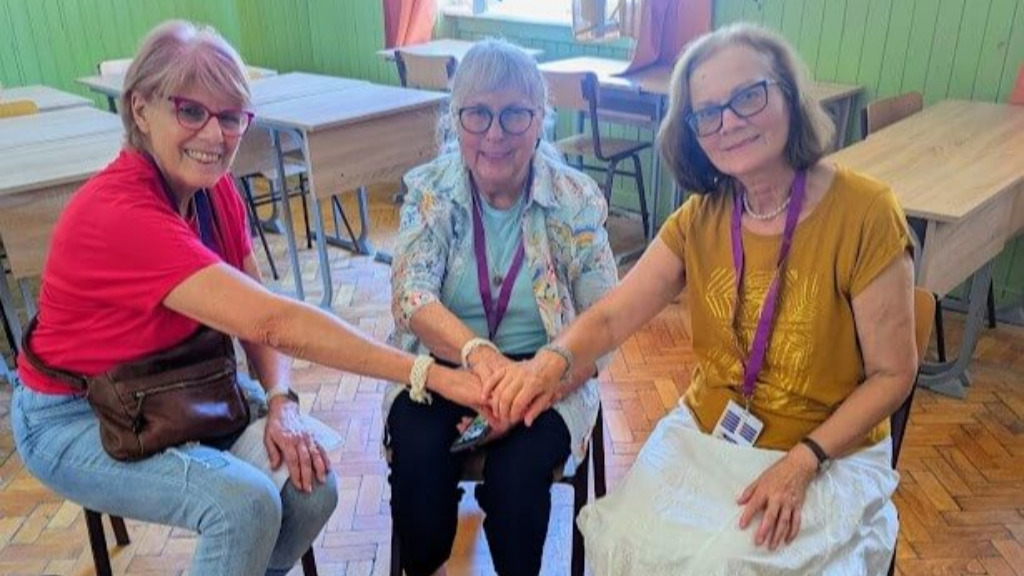 3 women sitting in a semi-circle with arms reaching out to touch in center